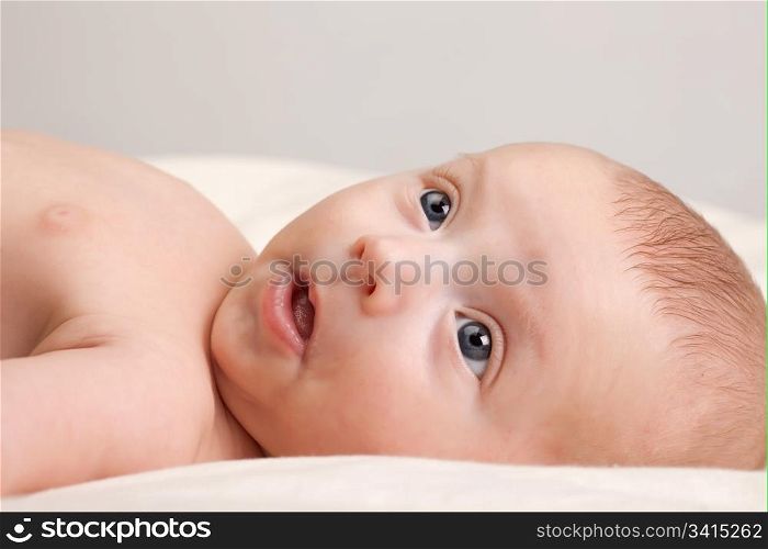 Ten weeks old cute little baby girl with curious look on her face lying comfortably on bed