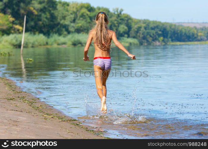 Ten year old girl runs along the riverbank, view from the back