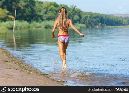 Ten year old girl runs along the riverbank, view from the back