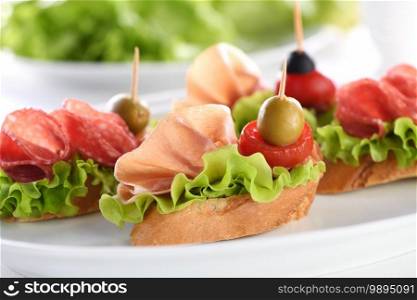 Tender baguette canapes with Leaf lettuce, salami or Parma ham, tomatoes, mozzarella and olive. Delicacy assorted platter for at the party.