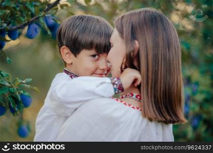 Tender scene of loving son embracing mom on plum orchard backdrop with sunlight. Beautiful family. Cute 4 years old kid with mother. Parenthood, childhood, happiness, children wellbeing concept.. Portrait of sweet family - 4 years old boy and mother in plum orchard