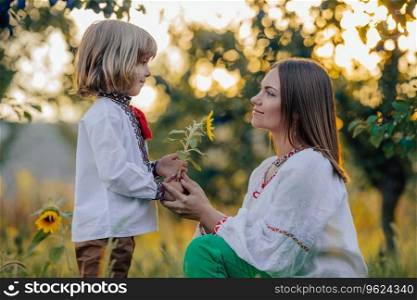 Tender scene of loving son with mom on apple garden backdrop with sunlight. Beautiful family. Cute 4 years old kid with mother. Parenthood, childhood, happiness, children wellbeing concept.. Portrait of beautiful family - 4 years old boy gives sunflower to mother, nature