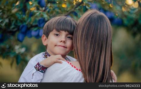 Tender scene of loving son with mom on plum orchard backdrop with sunlight. Beautiful family. Cute 4 years old kid with mother. Parenthood, childhood, happiness, children wellbeing concept.. Portrait of beautiful ukrainian family 4 years old boy, mother in plum orchard