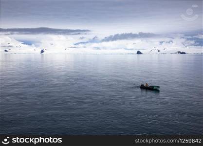 Tender Zodiac boat alone on sea in wide bay with white mountains all around in Antarctica
