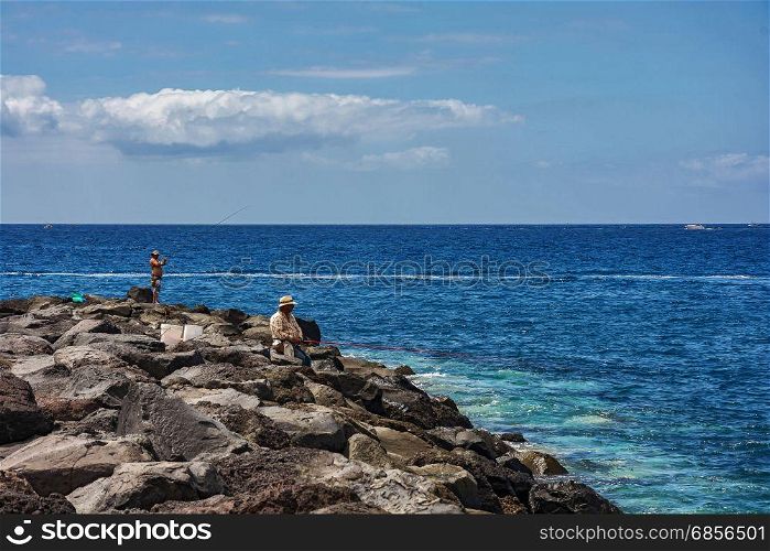Tenerife, Spain - 09/11/2016: On a stony shore, two men fish with fishing rods