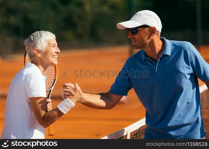 Tennis Activity Class for Senior People. Tennis Instructor with Senior Woman in her 60s Handshaking after Having a Tennis Lesson on Clay Court.