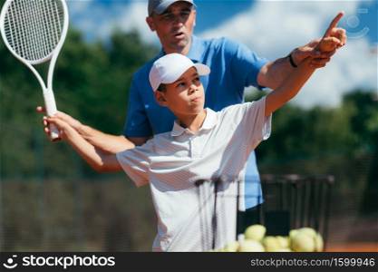 Tennis Coach Practicing Service with Boy on Tennis Class Outdoors.. Tennis Instructor Practicing Service with Junior Athlete