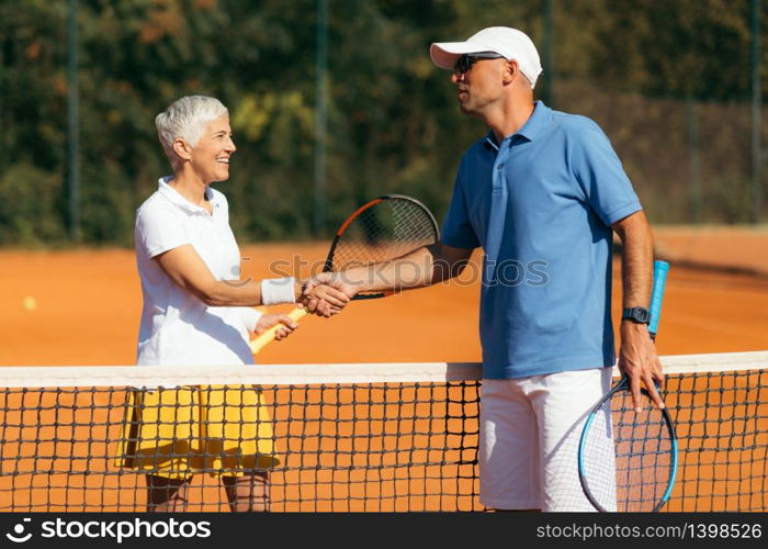 Tennis Instructor with Senior Woman in her 60s Handshaking after Having a Tennis Lesson on Clay Court.