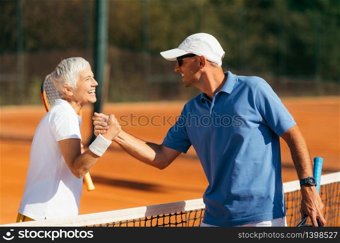 Tennis Instructor with Senior Woman in her 60s Handshaking after Having a Tennis Lesson on Clay Court.