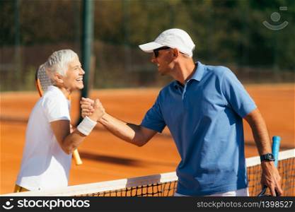 Tennis Instructor with Senior Woman in her 60s Handshaking after Having a Tennis Lesson on Clay Court.