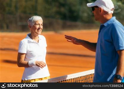Tennis Instructor with Senior Woman in her 60s Having a Tennis Lesson on Clay Court.