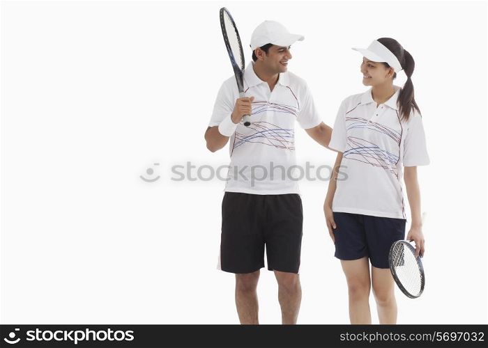 Tennis players looking at each other while holding rackets against white background