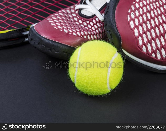 Tennis shoes, new ball, and racket on black background