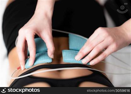 TENS, Transcutaneous Electrical Nerve Stimulation in Physical Therapy. Therapist Positioning Electrodes onto Patient&rsquo;s Lower Back. Therapist positioning electrodes onto a female athlete&rsquo;s lower back muscles