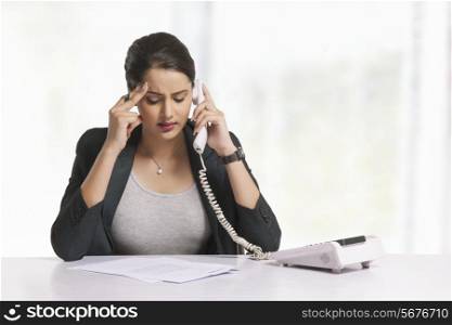 Tensed businesswoman answering telephone at office desk