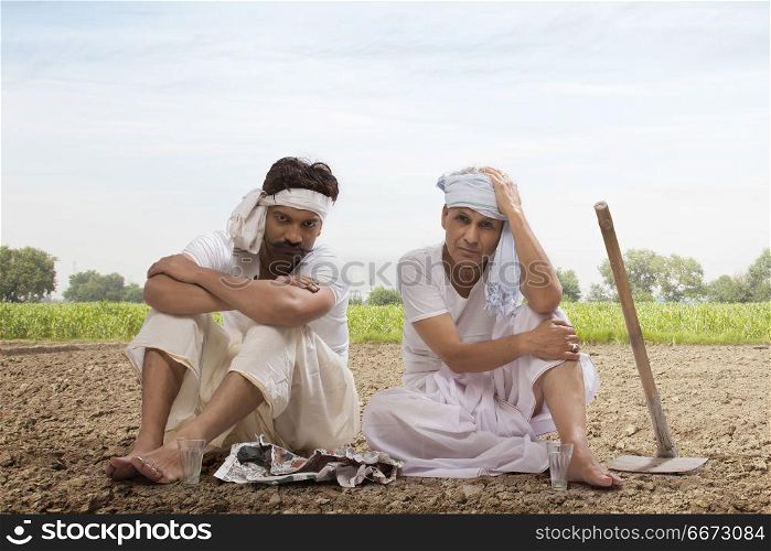 Tensed two farmers sitting in field drinking tea and eating snacks