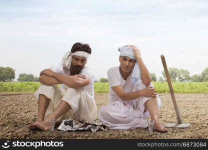 Tensed two farmers sitting in field drinking tea and eating snacks