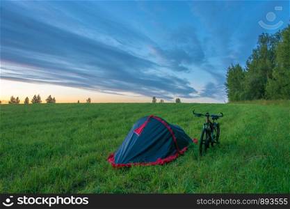 Tent and bike in the field on a summer evening at sunset.