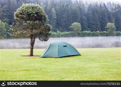 Tent on green grass lawn near the lake