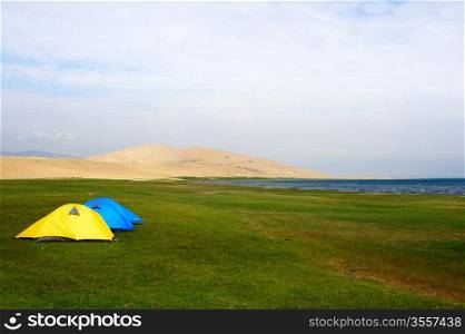 Tent on the lawn near the lake and sand dunes in qinghai province of China