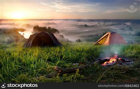 Tents and bonfire in steppe near river at sunrise