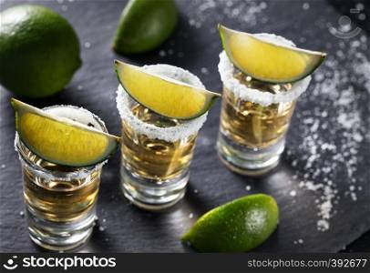Tequila glasses with lime and salt stand in row on black background. Alcoholic cocktail. Mexican traditional drink