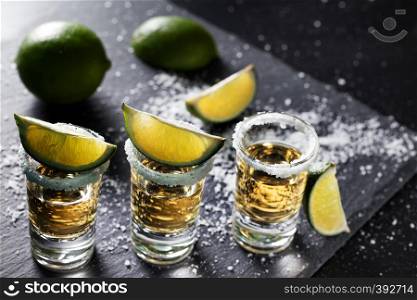 Tequila glasses with lime and spilled salt on a black background. Alcoholic cocktail. Mexican traditional drink
