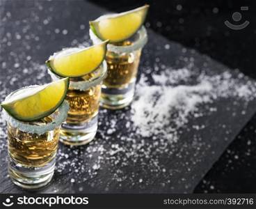 Tequila glasses with lime standing in row on black background. Alcoholic cocktail. Mexican traditional drink