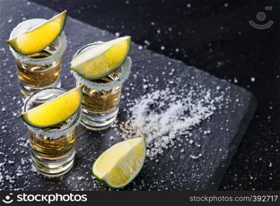 Tequila glasses with salt on the rim and lime on a black background? Alcoholic cocktail. Mexican traditional drink. Tequila glasses with salt on the rim and lime