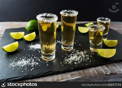 Tequila shots with lime on black stone background. Strong alcohol drink. Gold Mexican tequila shots. . Tequila shots with lime on black stone background