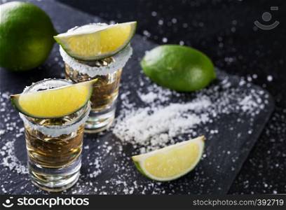 Tequila with sliced and whole lime and salt on a black background. Alcoholic cocktail. Mexican traditional drink. Tequila with sliced and whole lime and salt