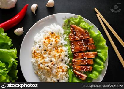 Teriyaki chicken with white rice on a plate. Tasty food and Chinese sticks on a dark background