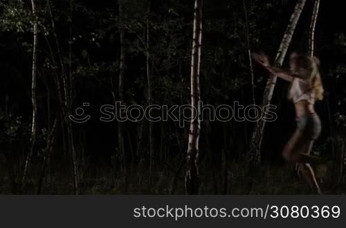 Terrified young woman in white t-shirt and shorts running away from the danger through the birch grove. Scared girl screaming and running through the dark forest from stranger. Slow motion.