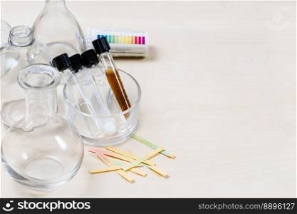 test tubes with various liquids, flasks and used litmus papers on light table with copyspace