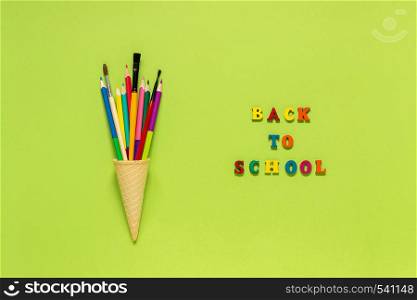 Text Back to school and colored pencils paintbrush in waffle ice cream cone on green paper background. Concept Education Flat lay Top view Template for postcard, lettering text or your design.. Text Back to school and colored pencils paintbrush in waffle ice cream cone on green paper background. Concept Education Flat lay Top view Template for postcard, lettering text or your design