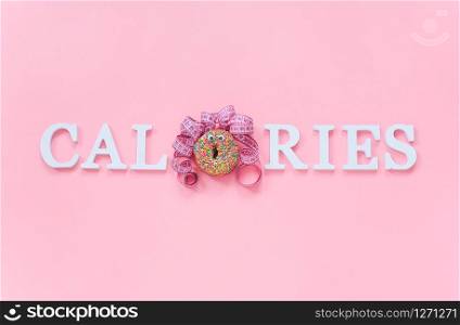 Text calories from volume letters and abstract funny face of woman from donut with eyes and hair from centimeter tape on pink background. Diet or unhealthy food concept Top view Flat lay Copy space.. Text calories from volume letters and abstract funny face of woman from donut with eyes and hair from centimeter tape on pink background. Diet or unhealthy food concept Top view Flat lay Copy space