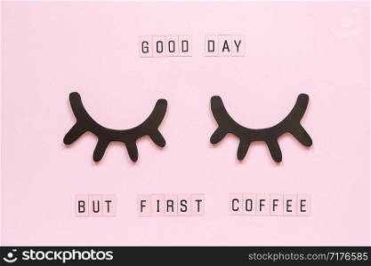 Text Good day, but first coffee and decorative wooden black eyelashes, closed eyes, on pastel pink paper background. Layout Top view Flat lay Concept good morning Template for postcard or design.. Text Good day, but first coffee and decorative wooden black eyelashes, closed eyes, on pastel pink paper background. Layout Top view Flat lay Concept good morning Template for postcard or design