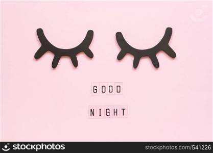 Text Good Night and decorative wooden black eyelashes, closed eyes on pink paper background. Concept Sweet dreams Greeting card Top view Creative flat lay.. Text Good Night and decorative wooden black eyelashes, closed eyes on pink paper background. Concept Sweet dreams Greeting card Top view Creative flat lay
