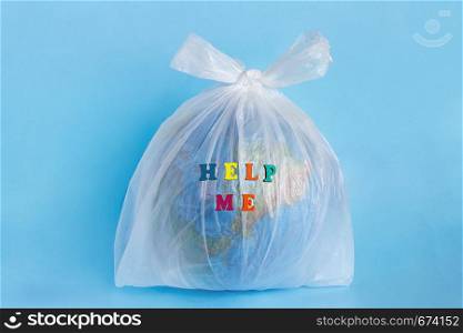 Text Help me and Model planet Earth in polyethylene plastic disposable package on blue background. Ecology problems Concept pollution of environment with polyethylene plastic waste World Earth Day. Help me and Model planet Earth in polyethylene plastic package