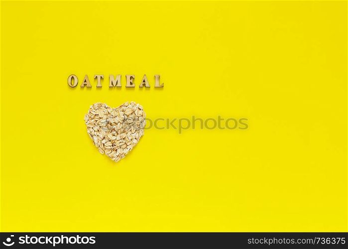 Text Oatmeal and oat flakes in shape heart on yellow background. Helthy organic diet concept. Top view Copy space. Text Oatmeal and oat flakes in the shape heart on yellow background.