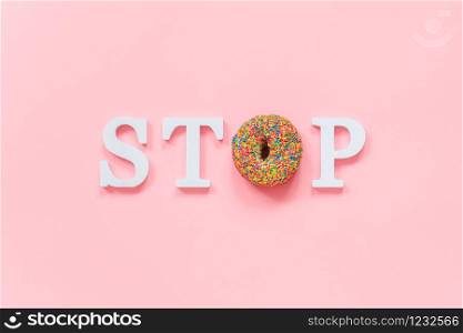 Text STOP from white volume letters and glazed colorful donut on pink background. Diet, refusal of fast food, unhealthy food Top view Flat lay Copy space.. Text STOP from white volume letters and glazed colorful donut on pink background. Diet, refusal of fast food, unhealthy food Top view Flat lay Copy space