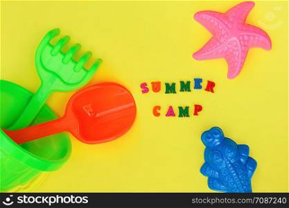 Text Summer camp and multicolored set children&rsquo;s toys for summer games in sandbox or on sandy beach on yellow background. Creative top view Flat lay Concept children&rsquo;s rest and development.. Text Summer camp and multicolored set children&rsquo;s toys for summer games in sandbox or on sandy beach on yellow background. Creative top view Flat lay Concept children&rsquo;s rest and development