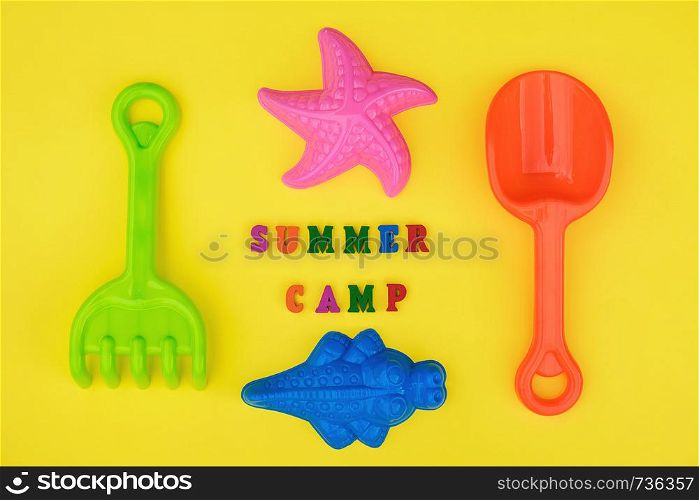 Text Summer camp and multicolored set children's toys for summer games in sandbox or on sandy beach on yellow background. Creative top view Flat lay Concept children's rest and development.. Text Summer camp and multicolored set children's toys for summer games in sandbox or on sandy beach on yellow background. Creative top view Flat lay Concept children's rest and development