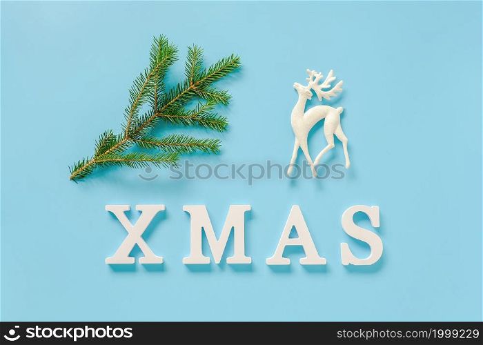 Text Xmas from white letters, green fir branch and christmas decoration deer toy on blue background. Concept Merry christmas. Minimal style Top view Flat lay Template for design, card, invitation.. Text Xmas from white letters, green fir branch and christmas decoration deer toy on blue background. Concept Merry christmas. Minimal style Top view Flat lay Template for design, card, invitation