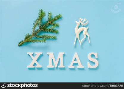 Text Xmas from white letters, green fir branch and christmas decoration deer toy on blue background. Concept Merry christmas. Minimal style Top view Flat lay Template for design, card, invitation.. Text Xmas from white letters, green fir branch and christmas decoration deer toy on blue background. Concept Merry christmas. Minimal style Top view Flat lay Template for design, card, invitation