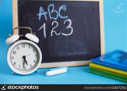 Textbooks and alarm clock on a blue background. Back to school. Library, education. Concept Education or business. Textbooks and alarm clock with school chalkboard on a blue background. Back to school. Concept Education or business