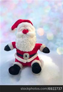Textile Santa Claus sitting on a snow bank, behind a blurred background with bokeh
