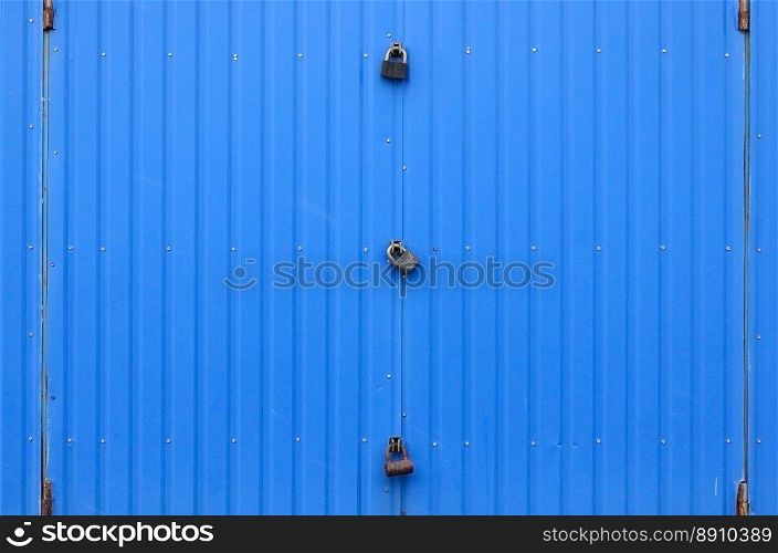 Texture of a metal blue wall with a gate closed for three locks