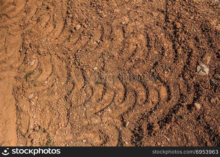 Texture of brown dirt with tractor tyre tracks.