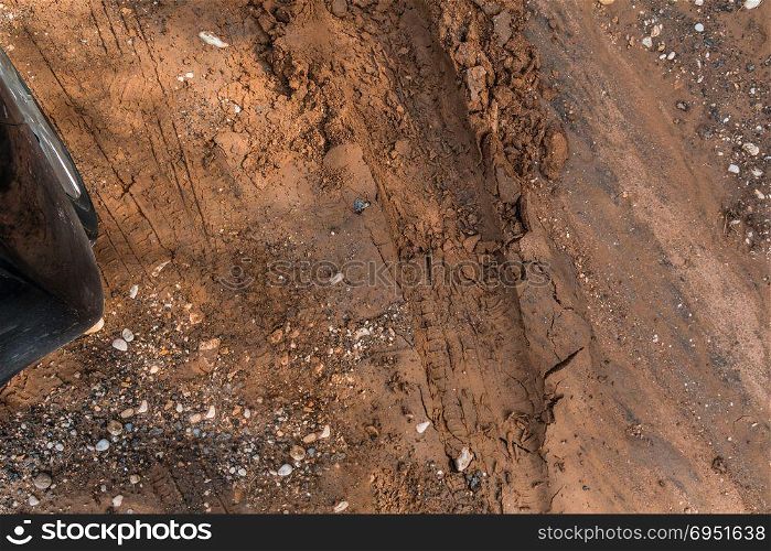 Texture of wet brown mud with car tyre tracks and shoe footprint